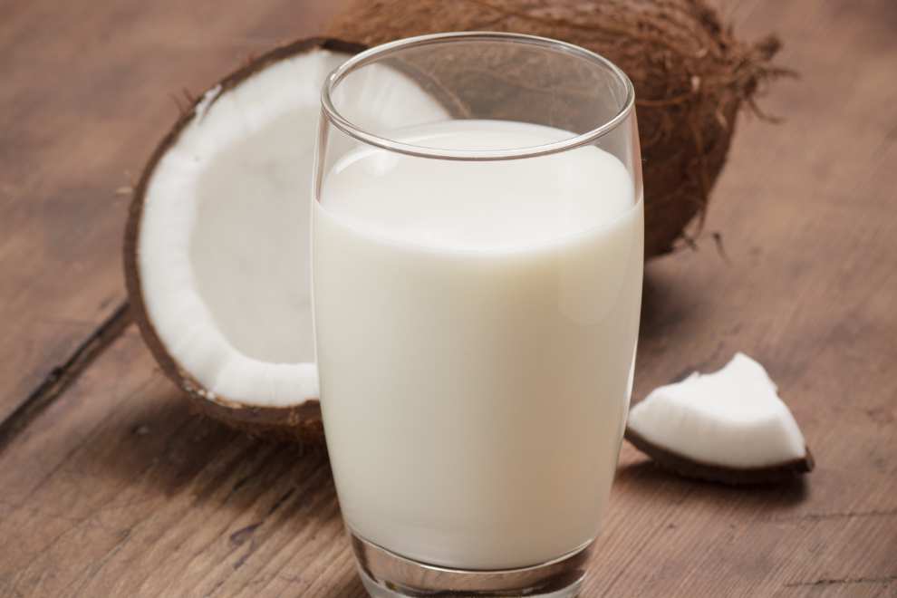 leite de coco em uma mesa de madeira com coco aberto ao lado