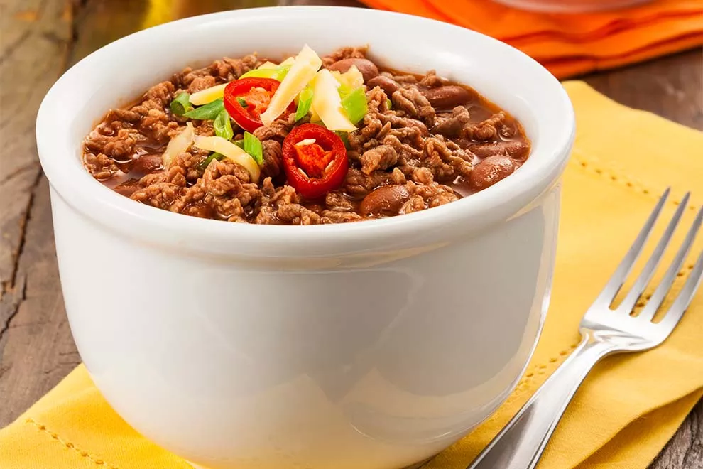 feijão mexicano de acém dentro de um pequeno bowl com um garfo ao lado em cima de um guardanapo amarelo em cima de uma mesa de madeira