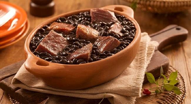 Feijoada servida em tigela marrom e rústica.