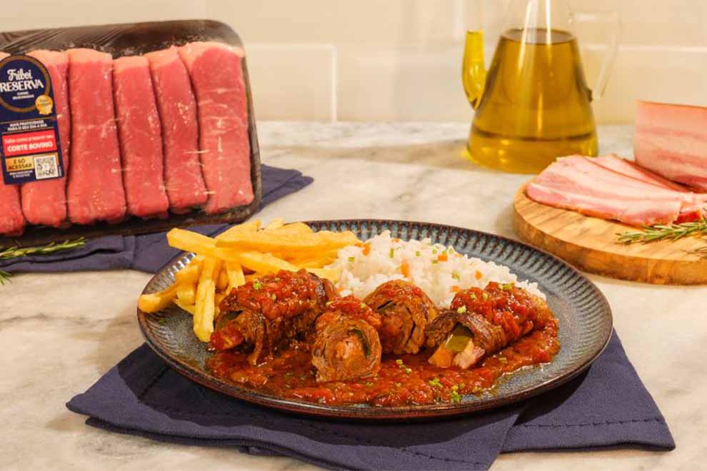 bife a role dentro de um prato de porcelana em cima de um pano azul escuro e em cima de uma mesa de madeira 