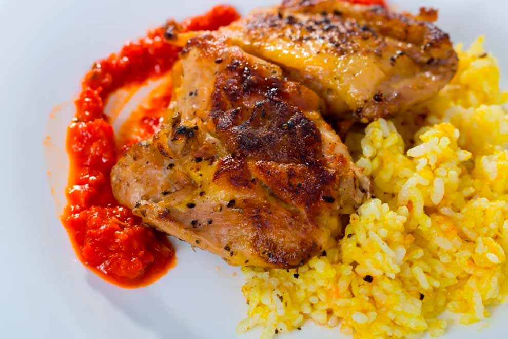 sobrecoxa temperado com arroz temperado em curry e amêndoas dentro de um prato branco de porcelana  