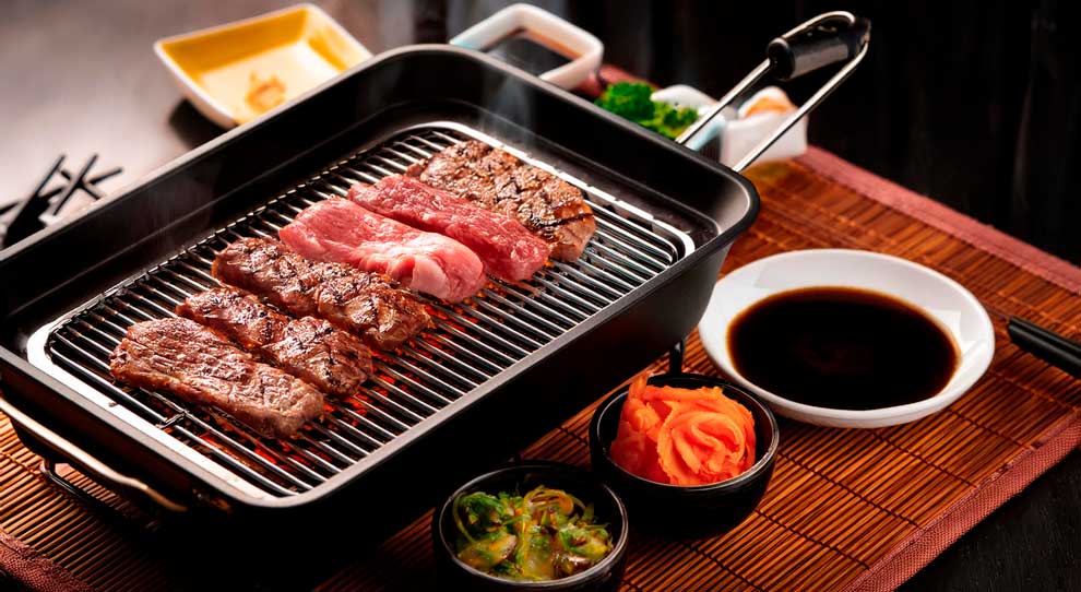 a imagem mostra uma grelha com 6 pedaços de carne em cima, abaixo tem uma tijela pequena com molho shoyu e outros dois potinhos