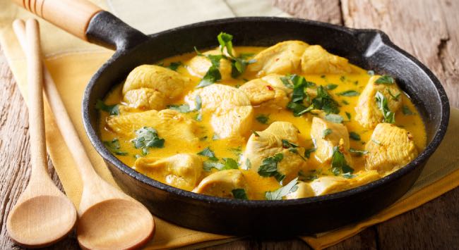 Panela preta e funda com uma generosa porção de uma receita de peito de frango com mandioca e leite de coco.