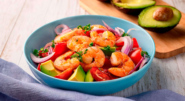 Salada de camarão servida com abacate em uma travessa azul.