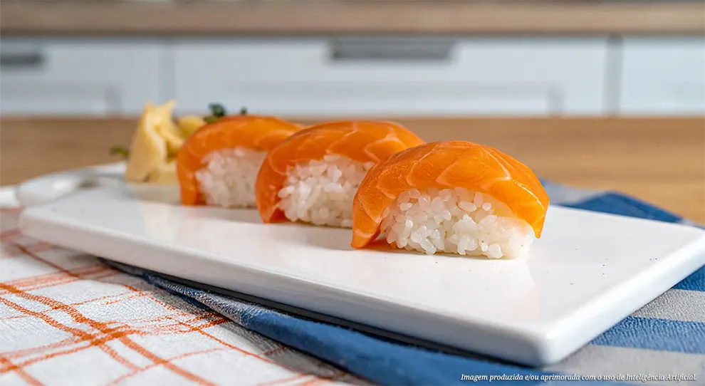 Três peças de niguiri de salmão, cada uma com uma fatia brilhante de salmão laranja sobre uma porção de arroz branco, dispostas em uma travessa branca retangular, acompanhadas de gengibre em conserva, sobre um pano de cozinha quadriculado laranja e branco com um guardanapo azul por baixo.