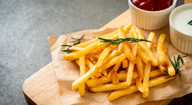 Porção de batata frita em um papel manteiga com potes de ketchup e maionese ao fundo.