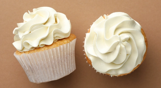 Dois bolinhos dourados e fofinhos, decorados com generosas camadas de chantilly branco.