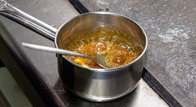 Calda de caramelo de pudim sendo preparada em uma panela de inox.