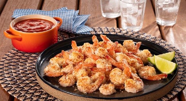 Camarões empanados no crispy de coco servidos com molho e limão cortado.