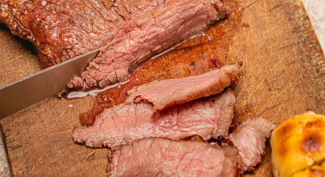 carne ao ponto sendo fatiada em uma tábua de madeira.