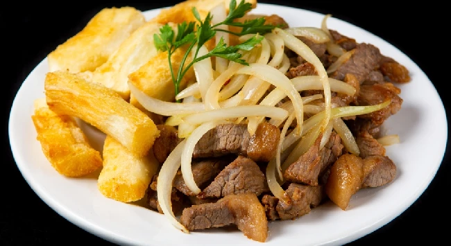 Carne de sol acebolada com mandioca frita em um prato branco.