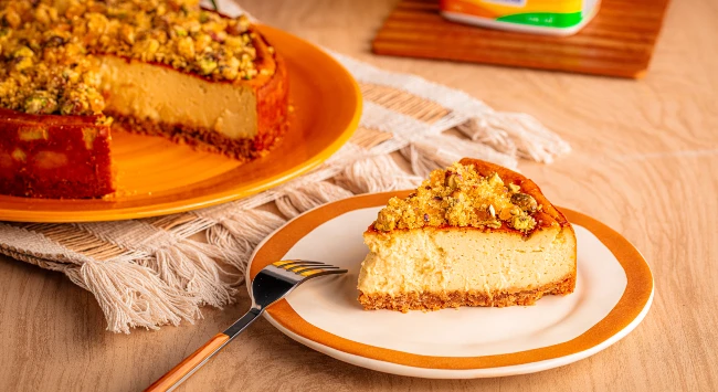 Fatia de cheescake de pistache servida em um prato branco com borda laranja.