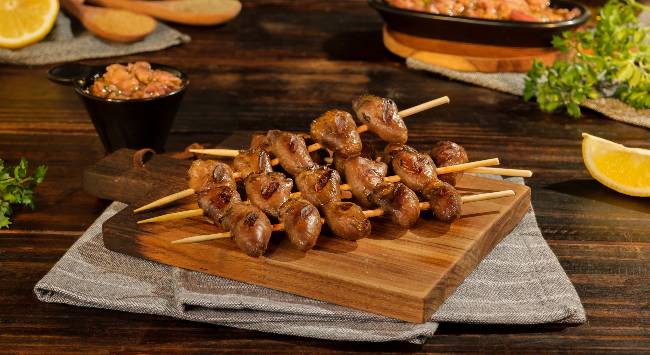 espetinhos de coração de frango servidos em tábua de madeira