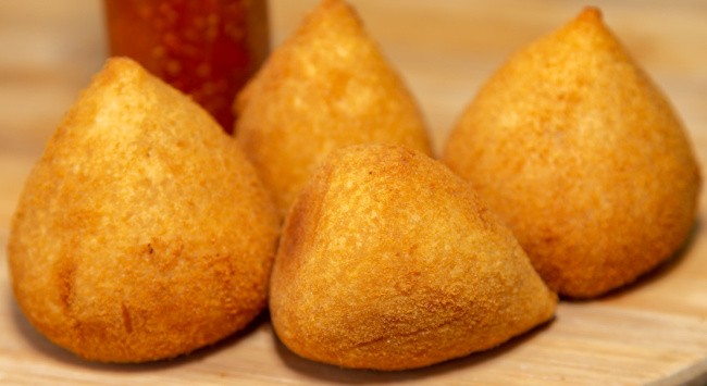 Coxinhas de frango empanadas e fritas em uma mesa de madeira.