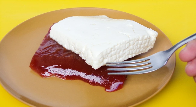 Queijo com goiabada cremosa servido em um prato laranja redondo.