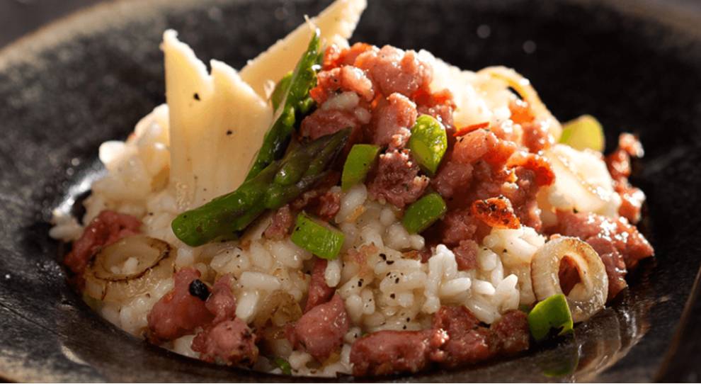 Imagem mostra um risoto de linguiça com ornamentos de queijo e tempero