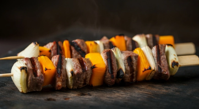 Espetinhos de carne com palmito e cubos de abóbora grelhados.