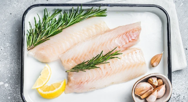 3 filés de peixe crus com limão, alho e alecrim em uma travessa.