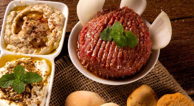 Porção de kibe cru temperado e servido com molho.