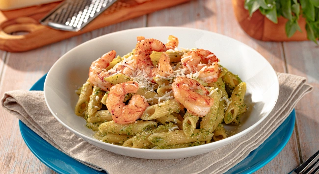Penne ao molho pesto com camarões grelhados, servido com queijo ralado, prato sofisticado e cheio de sabor.