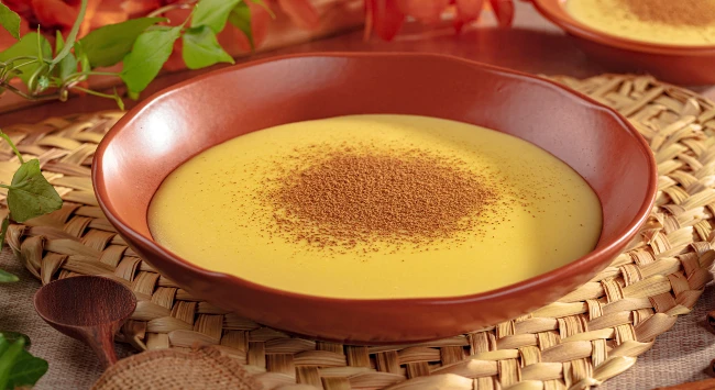 Mingau de milho verde servido com canela em uma tigela marrom.