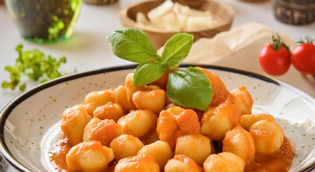 nhoque frito ao molho marinara servido em um prato branco e mesa decorada.
