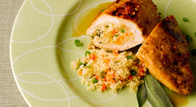 Porção de peito de frango com cuscuz marroquino servido em um prato verde redondo com detalhes brancos.
