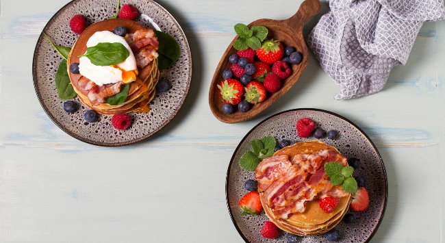 Panquecas americanas servidas com frutas e fatias de bacon.