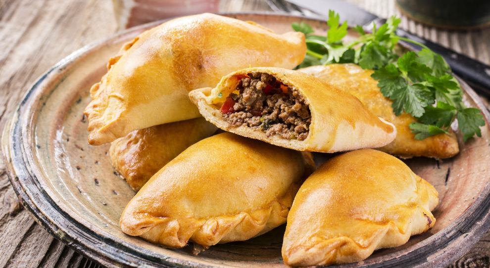Pastel de forno recheado com carne moída, servido em um prato bege redondo com mais 4 pasteis.