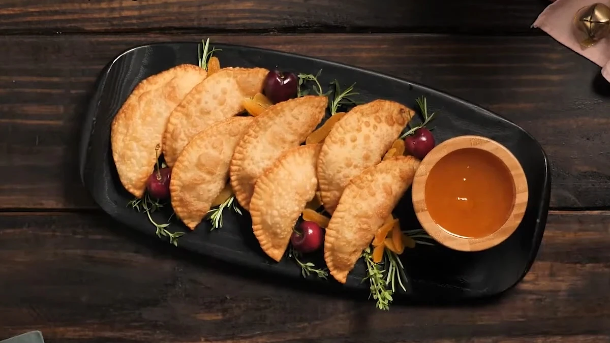 Pastel frito servido com gelea de damasco e decorações natalinas em uma tábua de petiscos preta.