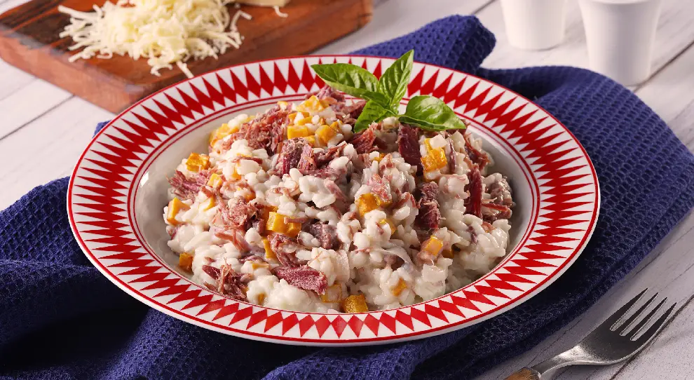 Risoto de carne seca desfiada com cubos de abóbora, servido em um prato com decoração vermelhos.