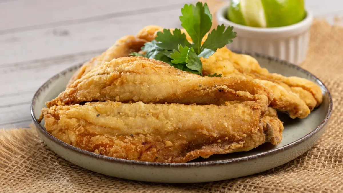sardinha frita empanada servida em um prato redondo com folhas de coentro por cima