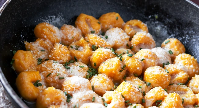 imagem da receita de sobrecoxa de Frango Seara DaGranja com Nhoque de Abóbora ao Molho Branco servida em um prato preto e decorado com queijo ralado.
