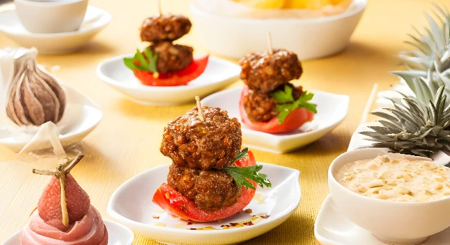 Fatias de tomate com duas almôndegas espetadas com um palito.