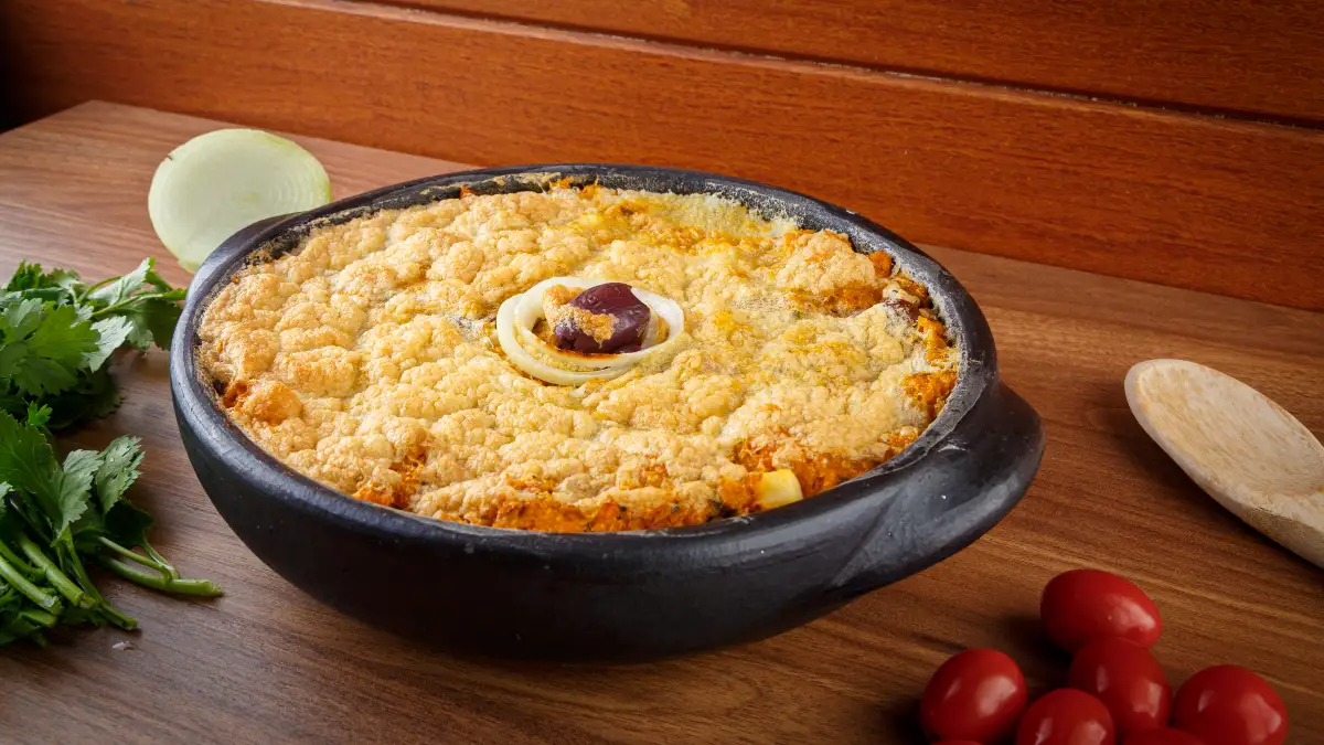 Torta capixaba servida em uma panela de pedra em uma mesa de madeira.